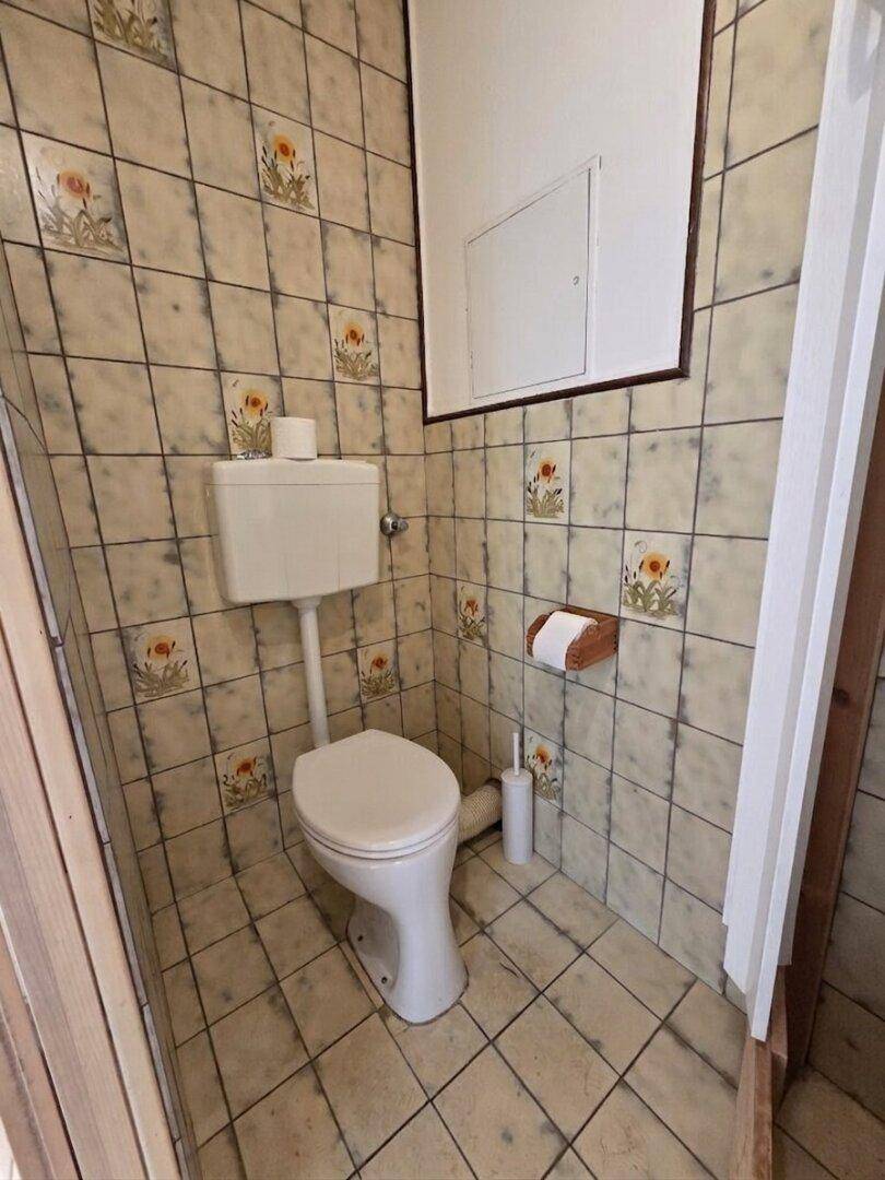 Separate Toilette mit gemusterten Fliesen und einem einfachen WC-Becken.
