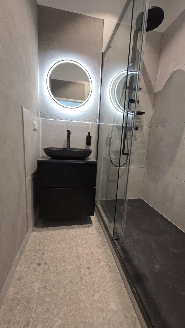 Modernes Badezimmer mit schwarzem Waschbecken, beleuchtetem Spiegel und einer geräumigen begehbaren Dusche.