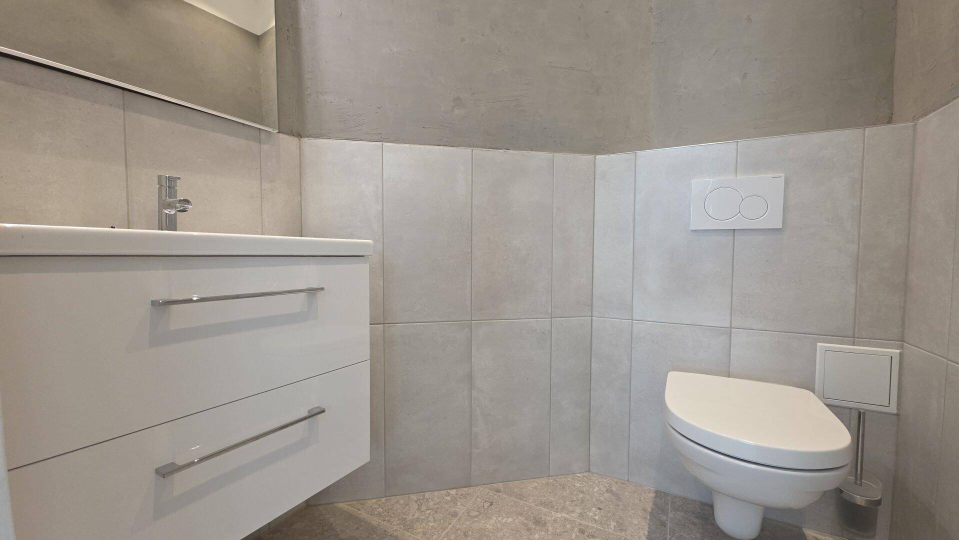 Modernes WC mit wandhängender Toilette und einem weißen Waschtisch mit integriertem Waschbecken.