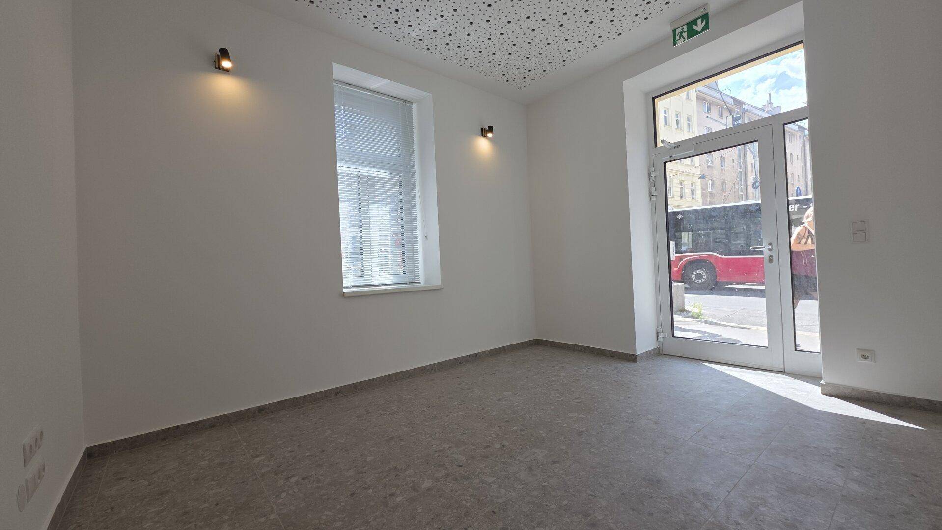 Heller, leerer Geschäftsraum mit großen Fenstern und einer Glastür zur belebten Straße.