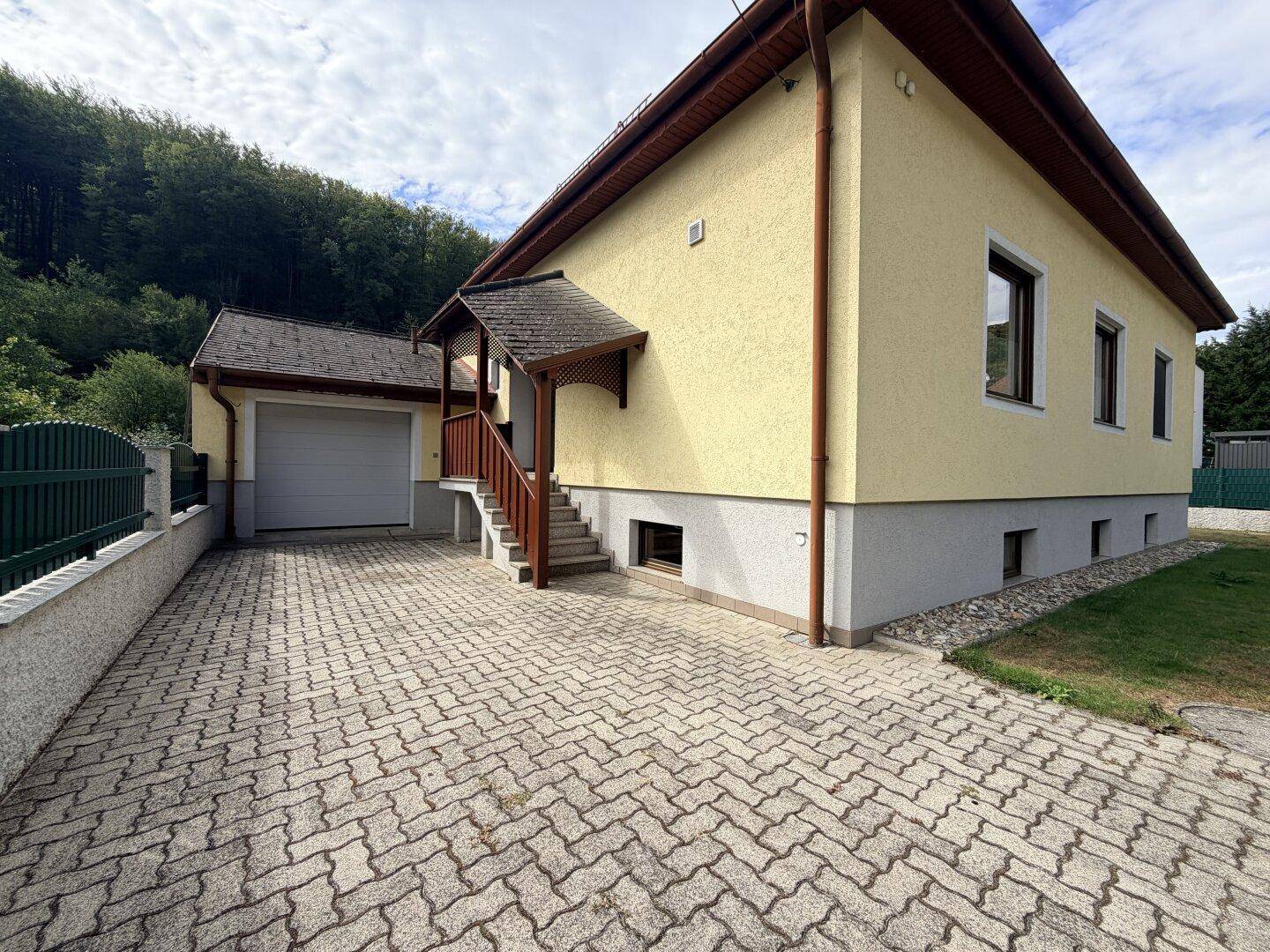 Einfamilienhaus mit gepflasterter Auffahrt, integrierter Garage und Zugang zum Eingangsbereich.