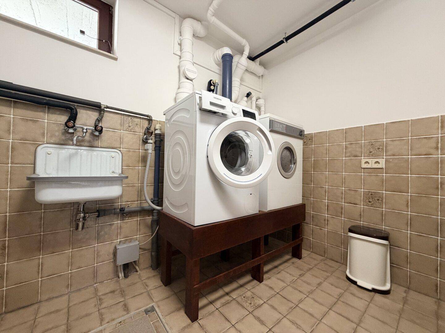Praktische Waschküche mit Waschmaschine, Trockner, Waschbecken und Fliesenboden.