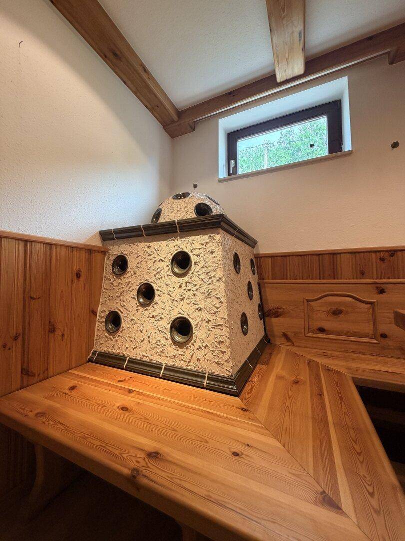 Traditioneller Raum mit Kachelofen, Holzbalken und gemütlichen Holzbänken, rustikaler Charme.