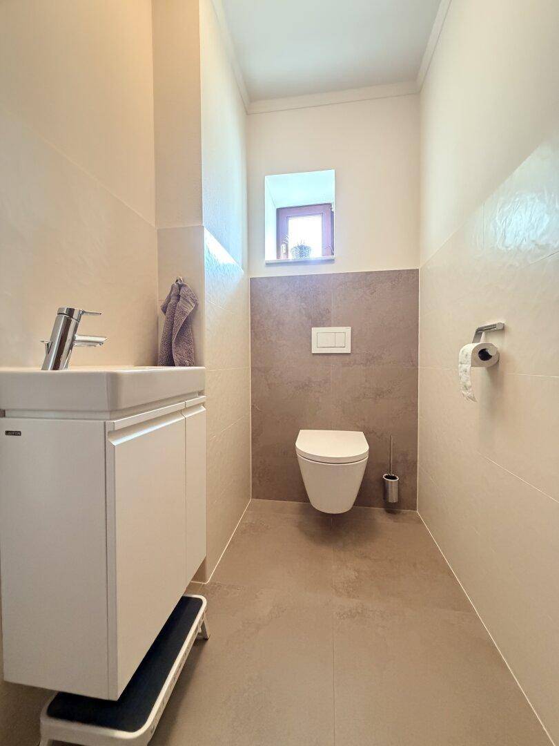 Modernes Gäste-WC mit wandhängendem WC, kleinem Waschbecken und Fenster für Tageslicht.