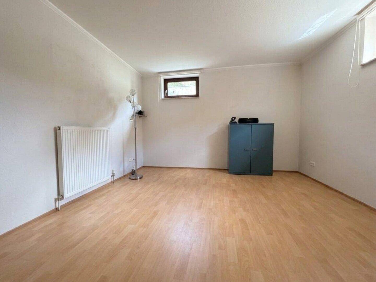 Geräumiger Kellerraum mit Laminatboden, Heizkörper und Fenster, vielseitig nutzbar.