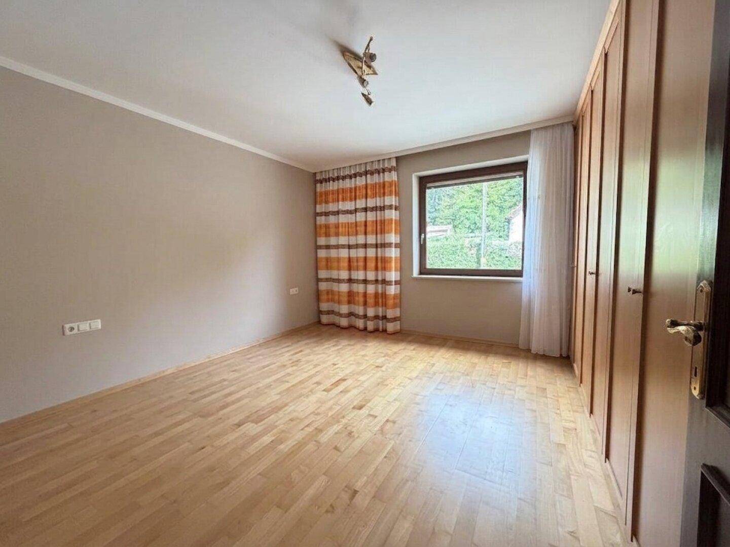 Gemütliches Schlafzimmer mit hellem Holzboden, Einbauschränken und Blick ins Grüne.