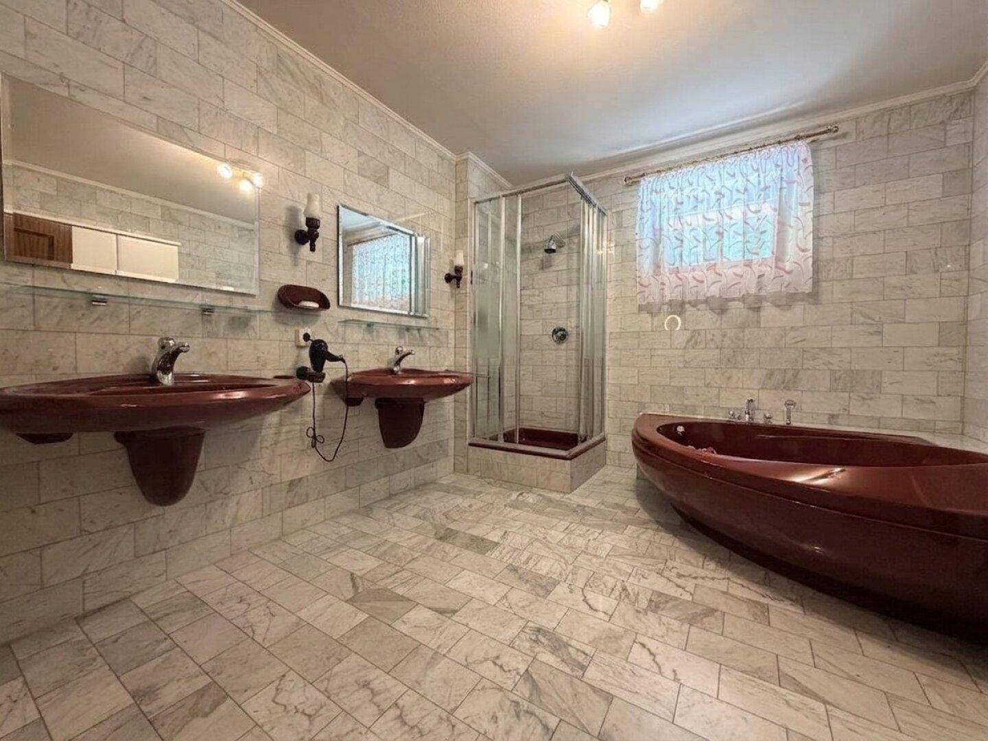 Badezimmer im Stil der 80er Jahre mit Dusche, zwei Waschbecken und farbiger Badewanne.