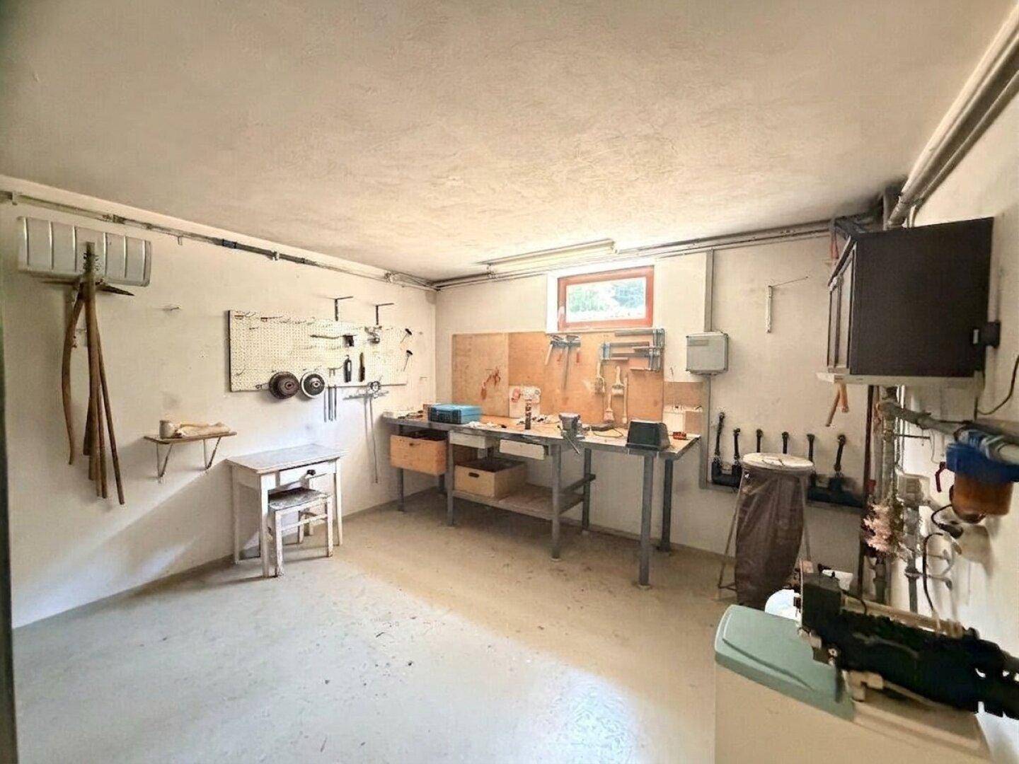Funktionale Werkstatt im Keller mit Arbeitsbank, Werkzeugen und Fenster für natürliche Belichtung.