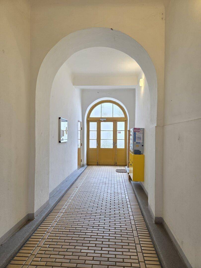 Eingangsbereich des Gebäudes mit gewölbter Decke, Fliesenboden und gelben Türen.