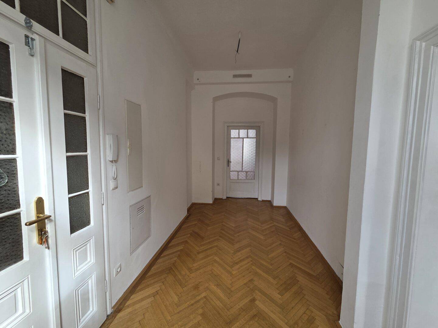 Langer Flur mit Fischgrätparkett und einer klassischen Eingangstür mit Glaseinsätzen.