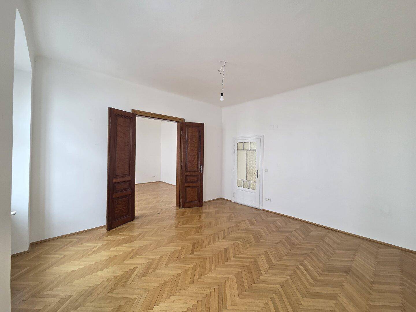 Helles Wohnzimmer mit klassischem Fischgrätparkett und hohen Decken, typisch für Altbauwohnungen.
