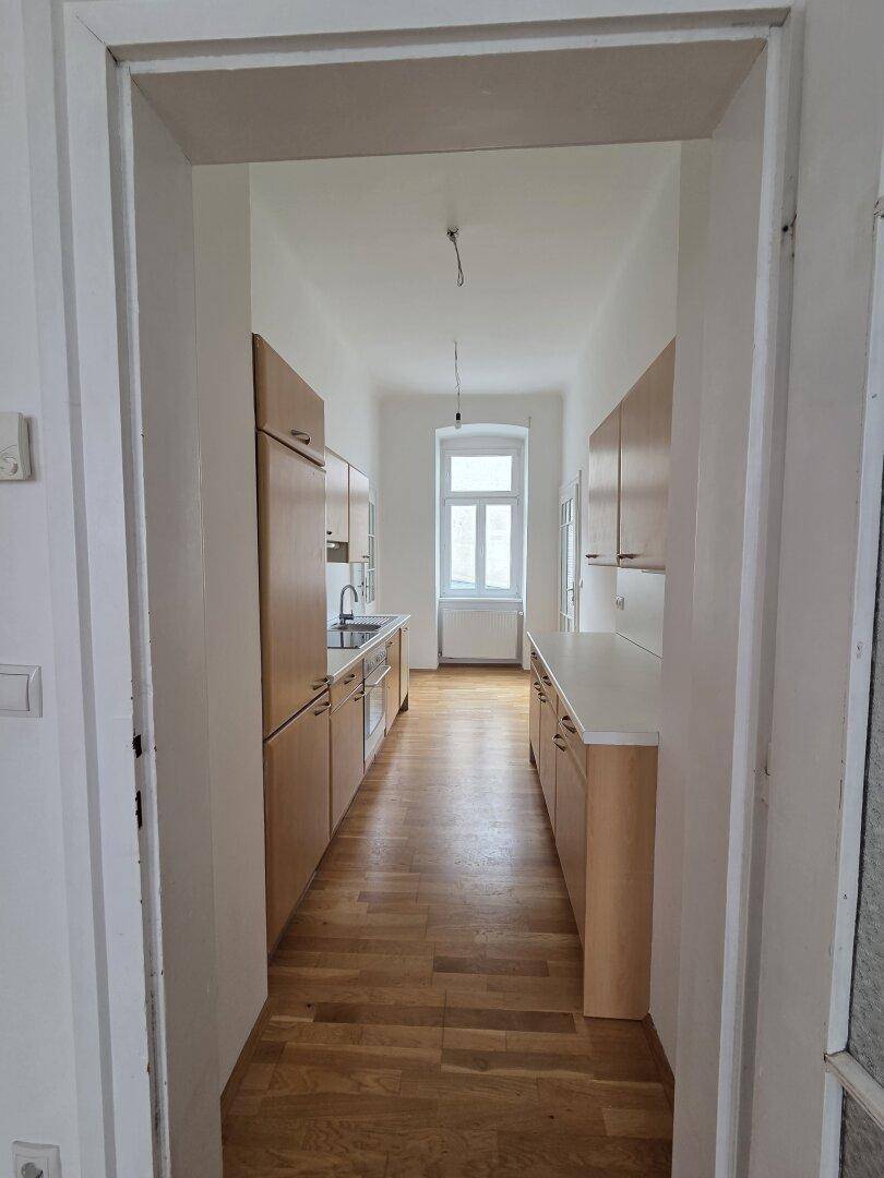 Längliche Küche mit beidseitigen Einbauschränken und Fenster am Ende des Raumes.