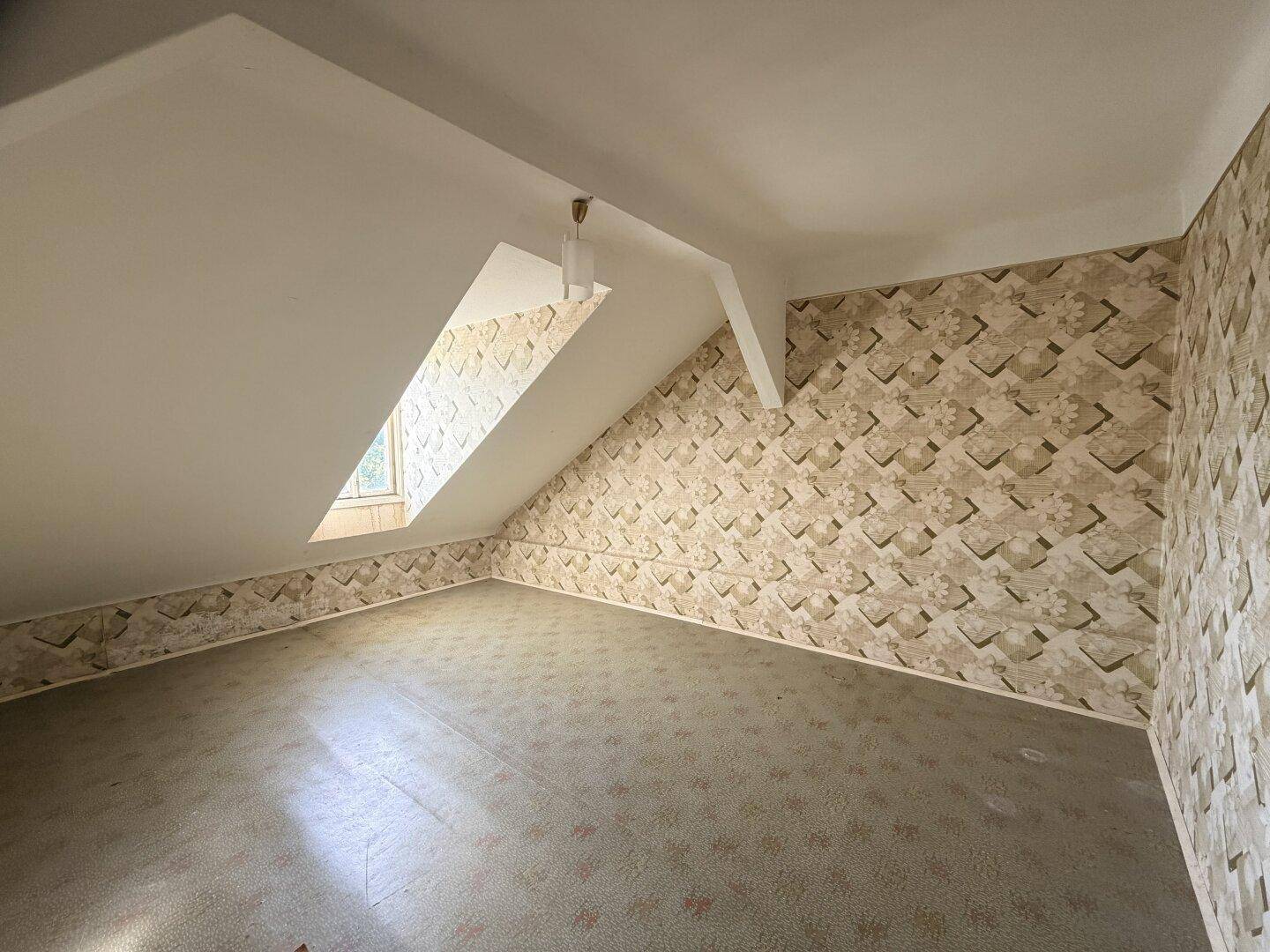 Dachgeschosszimmer mit schrägen Wänden und gemusterter Tapete, bietet Ausbaupotenzial.