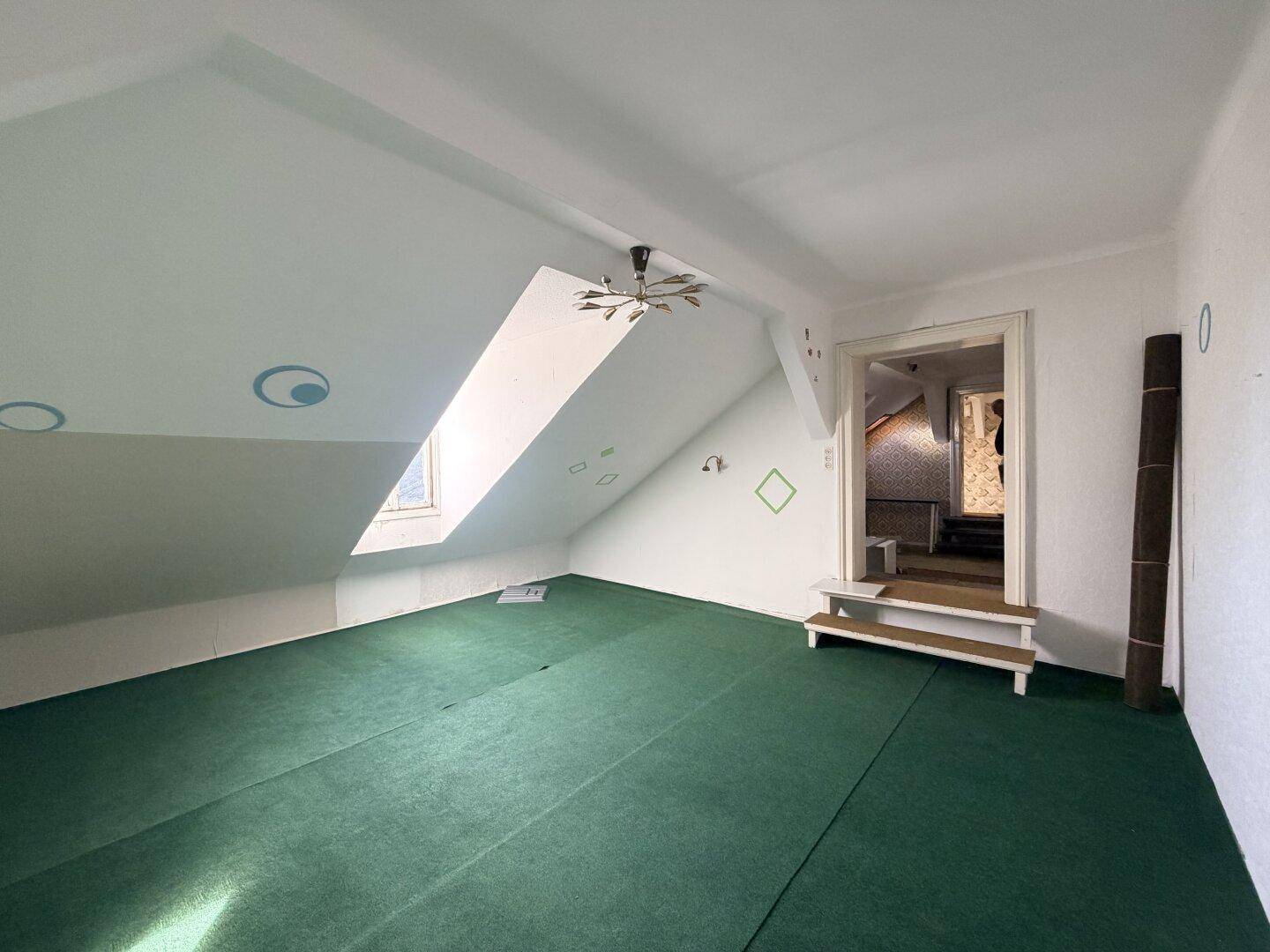 Geräumiges Dachgeschosszimmer mit grünem Teppichboden und schrägen Wänden.