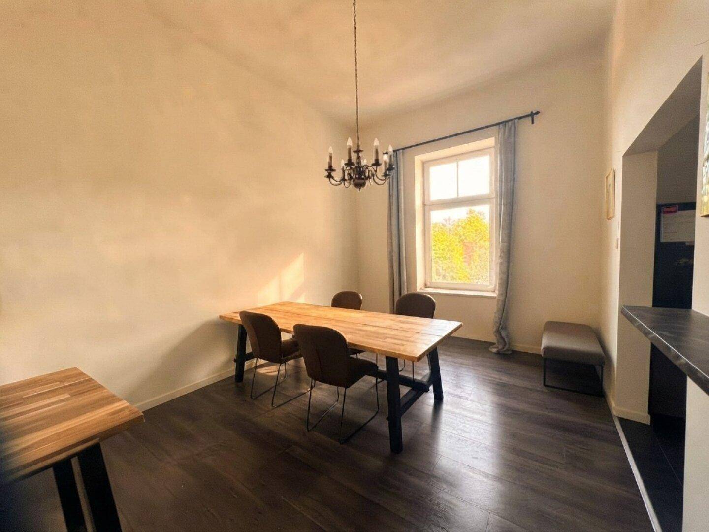 Heller Essbereich mit Holztisch, Stühlen und einem Fenster mit Blick ins Grüne.