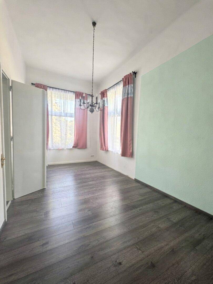 Helles Zimmer mit dunklem Laminatboden und einer mintgrünen Akzentwand.
