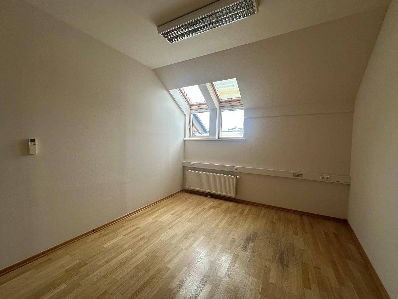 Helles Zimmer mit Holzboden, Dachfenstern und einem Heizkörper, ideal für ein Büro oder Schlafzimmer.