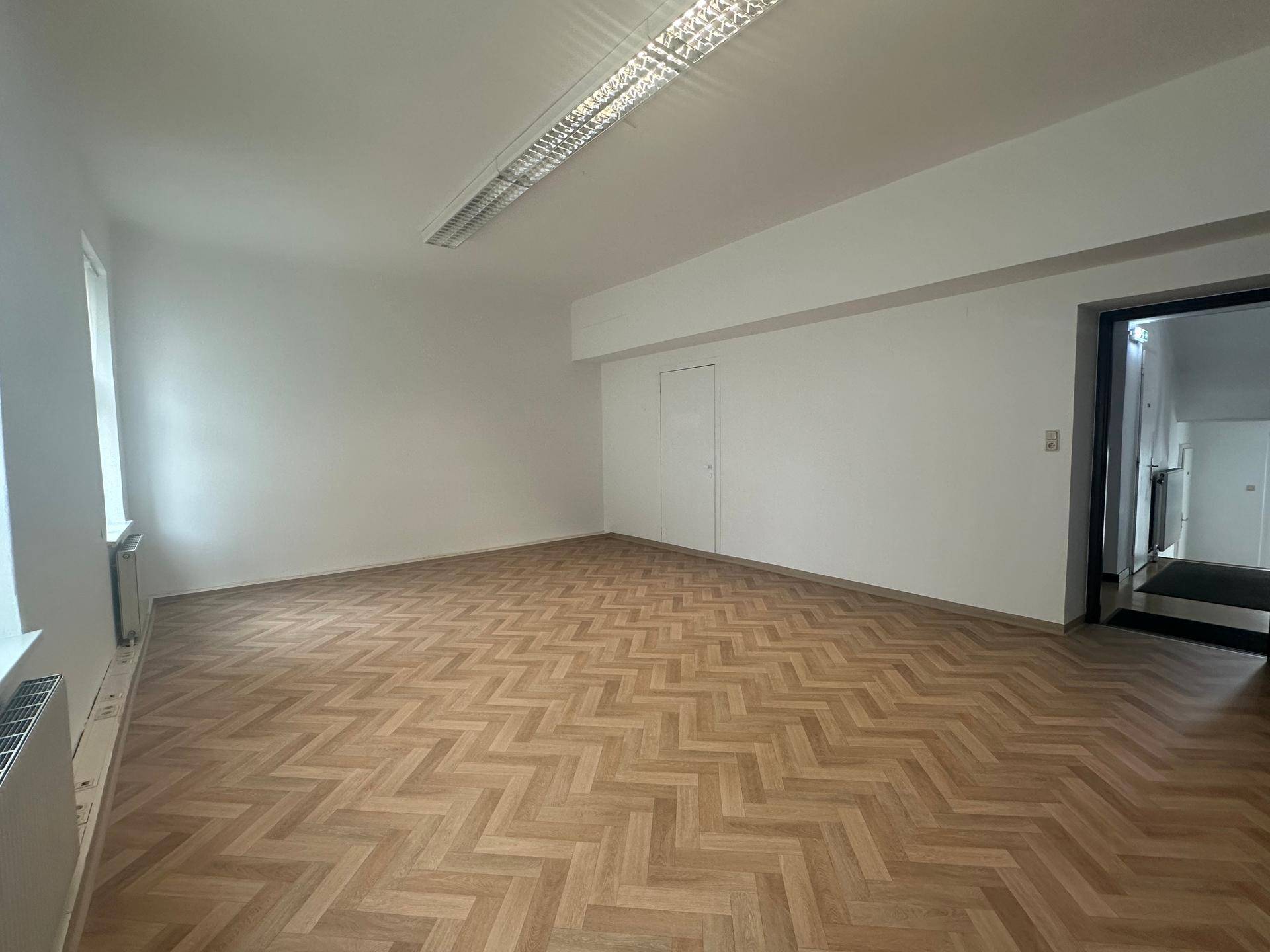 Heller Büroraum mit Fischgrätparkett und weiß gestrichenen Wänden, bereit zur individuellen Gestaltung.
