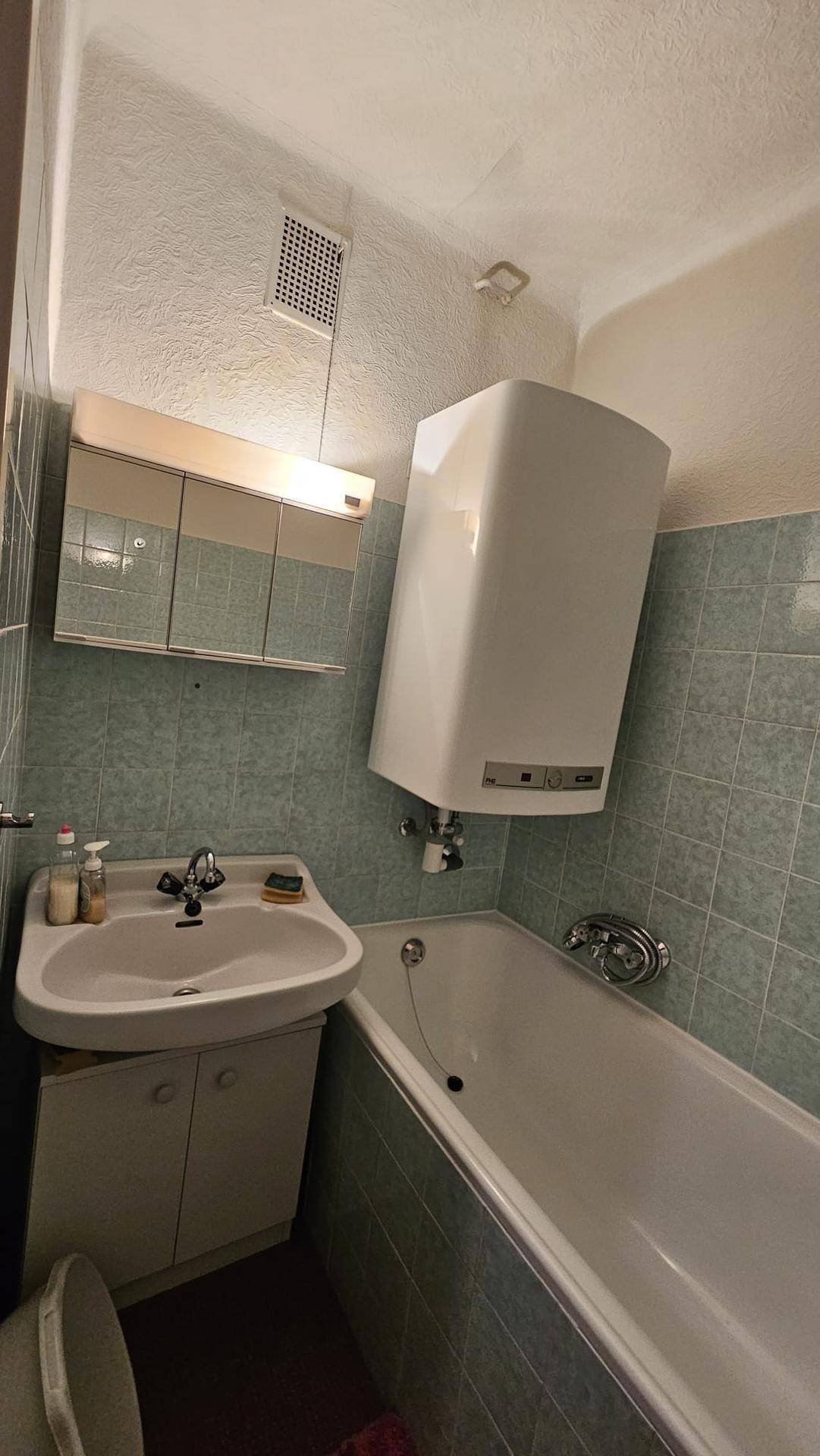 Kleines Badezimmer mit Badewanne, Waschbecken und einem Wandboiler über der Wanne.