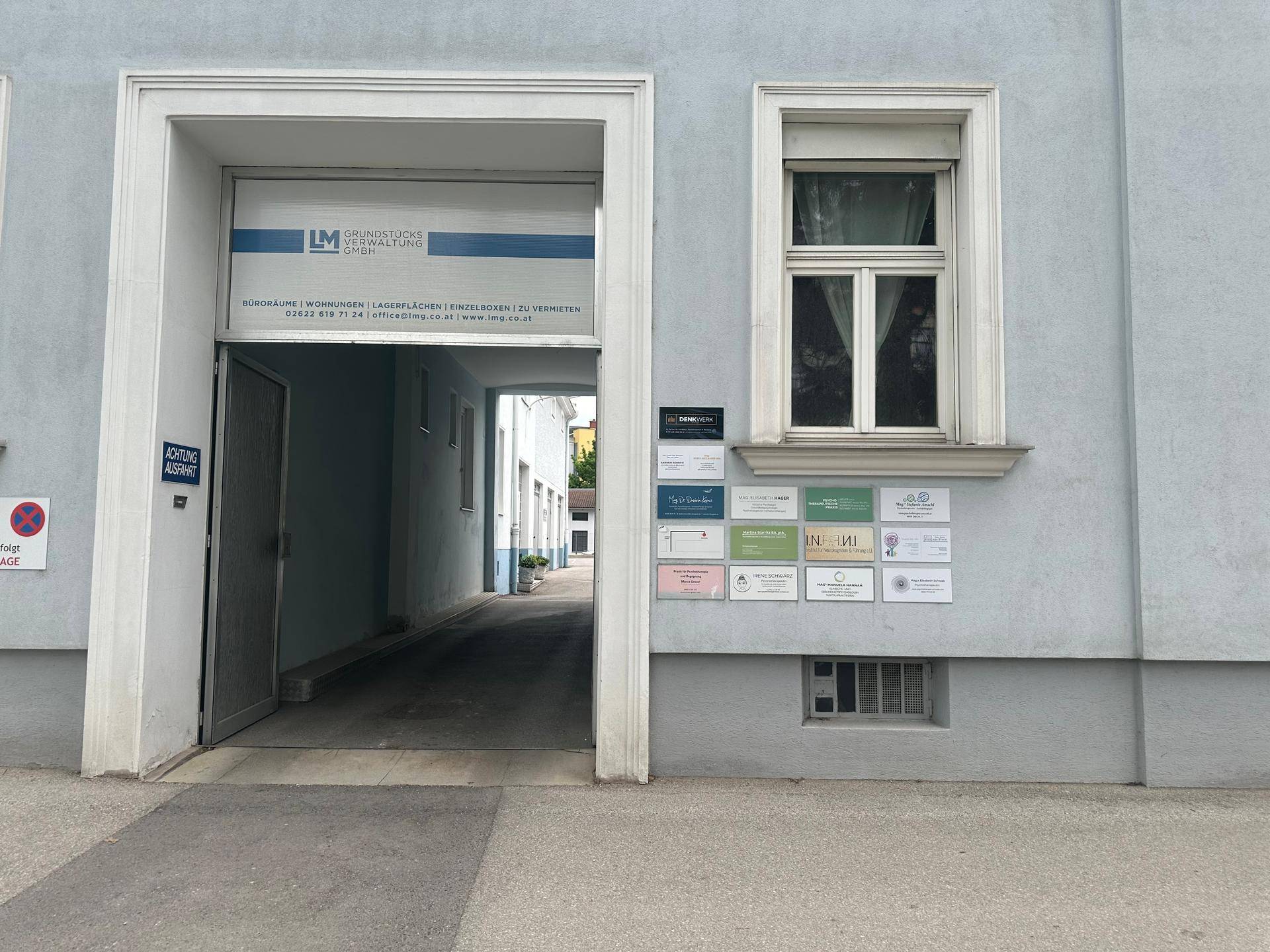 Eingangsbereich eines Gebäudes mit Durchfahrt und mehreren Firmenschildern an der Fassade.