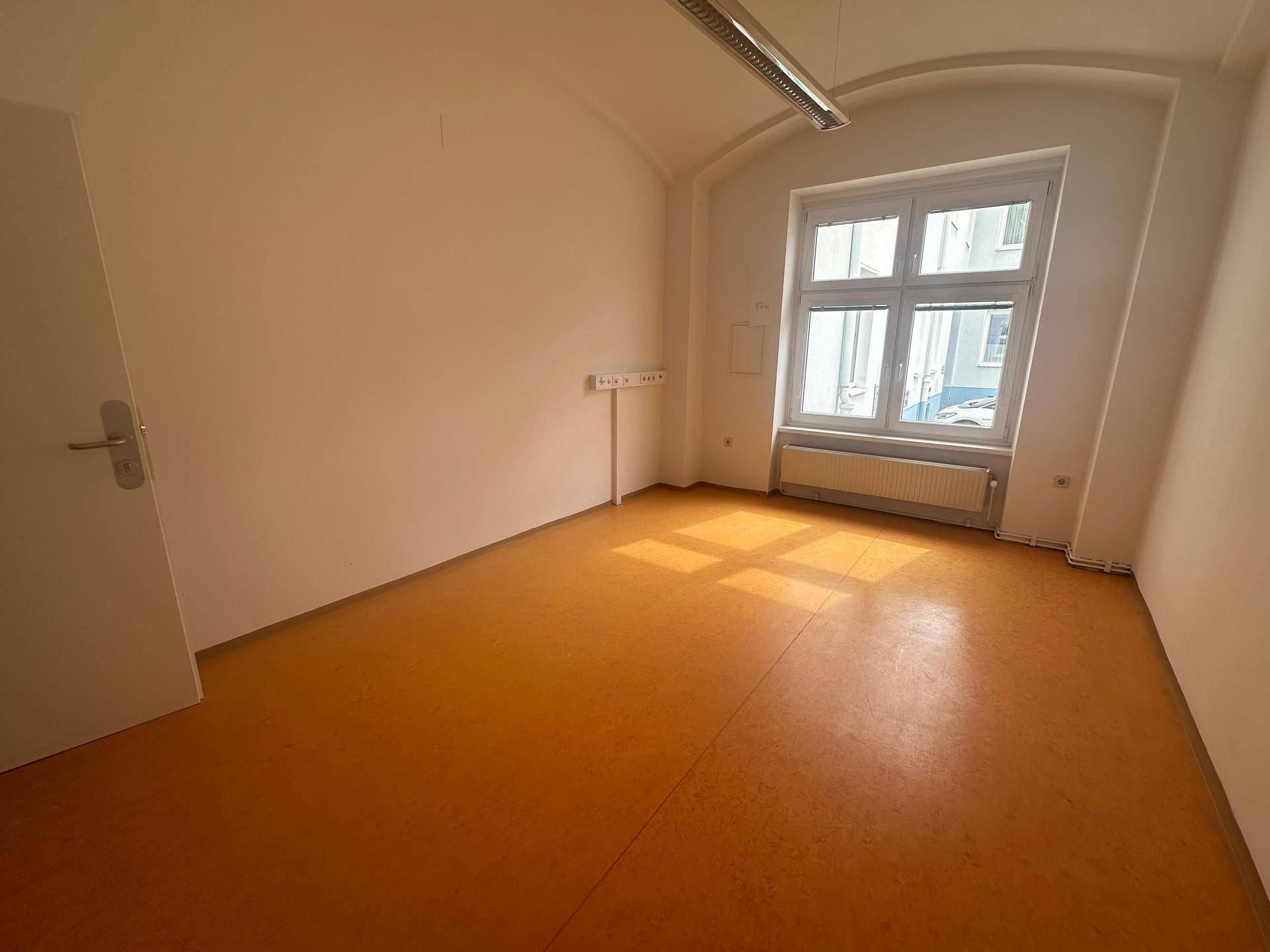 Heller Büroraum mit orangefarbenem Linoleumboden und großem Fenster, das viel Licht spendet.