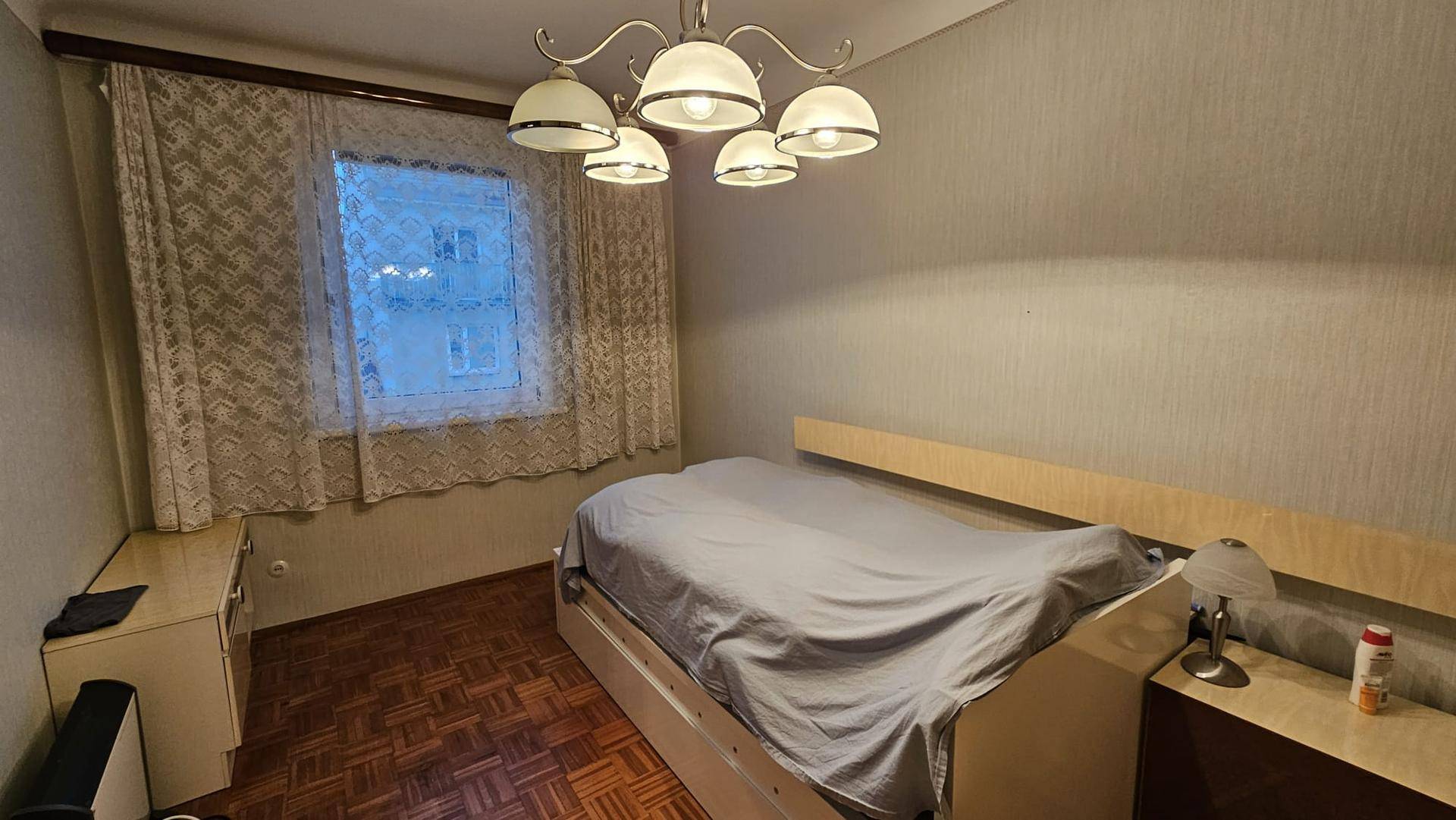 Schlafzimmer mit Einzelbett, Parkettboden und einem Fenster mit Vorhängen für natürliches Licht.