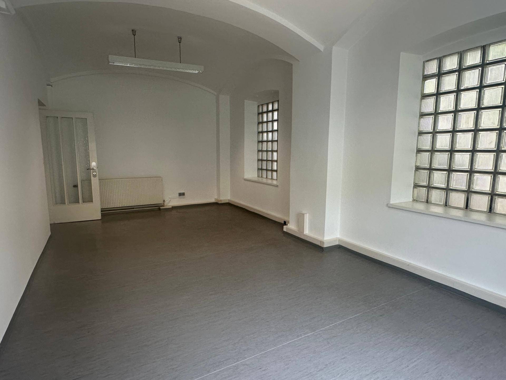Geräumiger Raum mit dunklem Boden, Glasbausteinfenstern und gewölbter Decke, ideal für verschiedene Nutzungen.