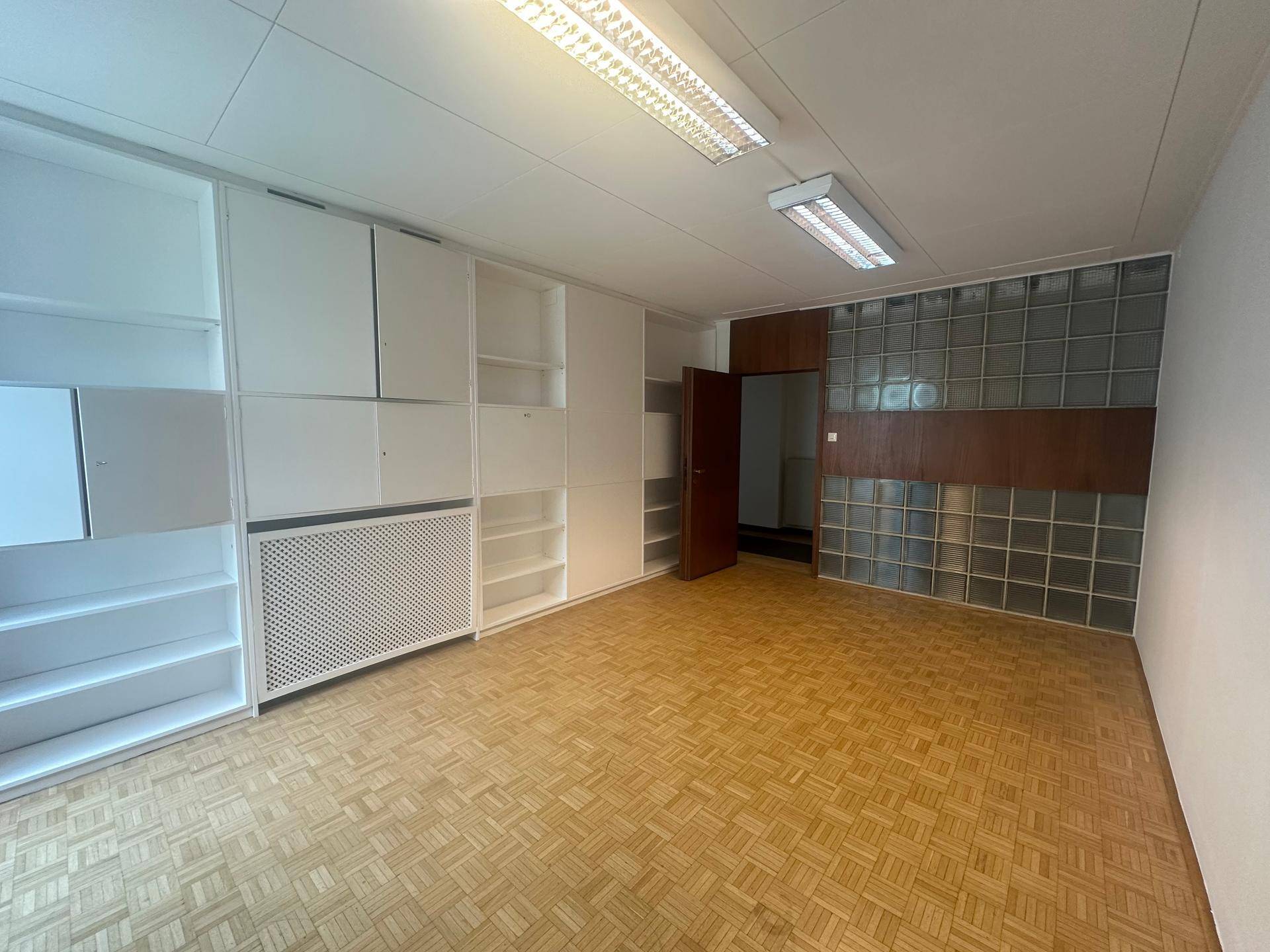 Büroraum mit integrierten weißen Regalen, Glasbausteinwand und Holzparkett, bietet viel Stauraum.