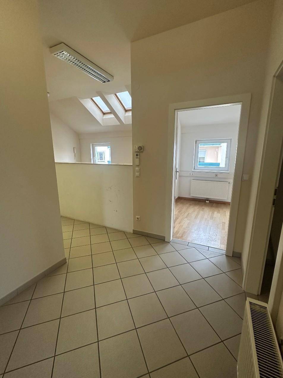 Heller Flur mit Fliesenboden und Blick in ein angrenzendes Zimmer mit Holzboden und Dachfenstern.