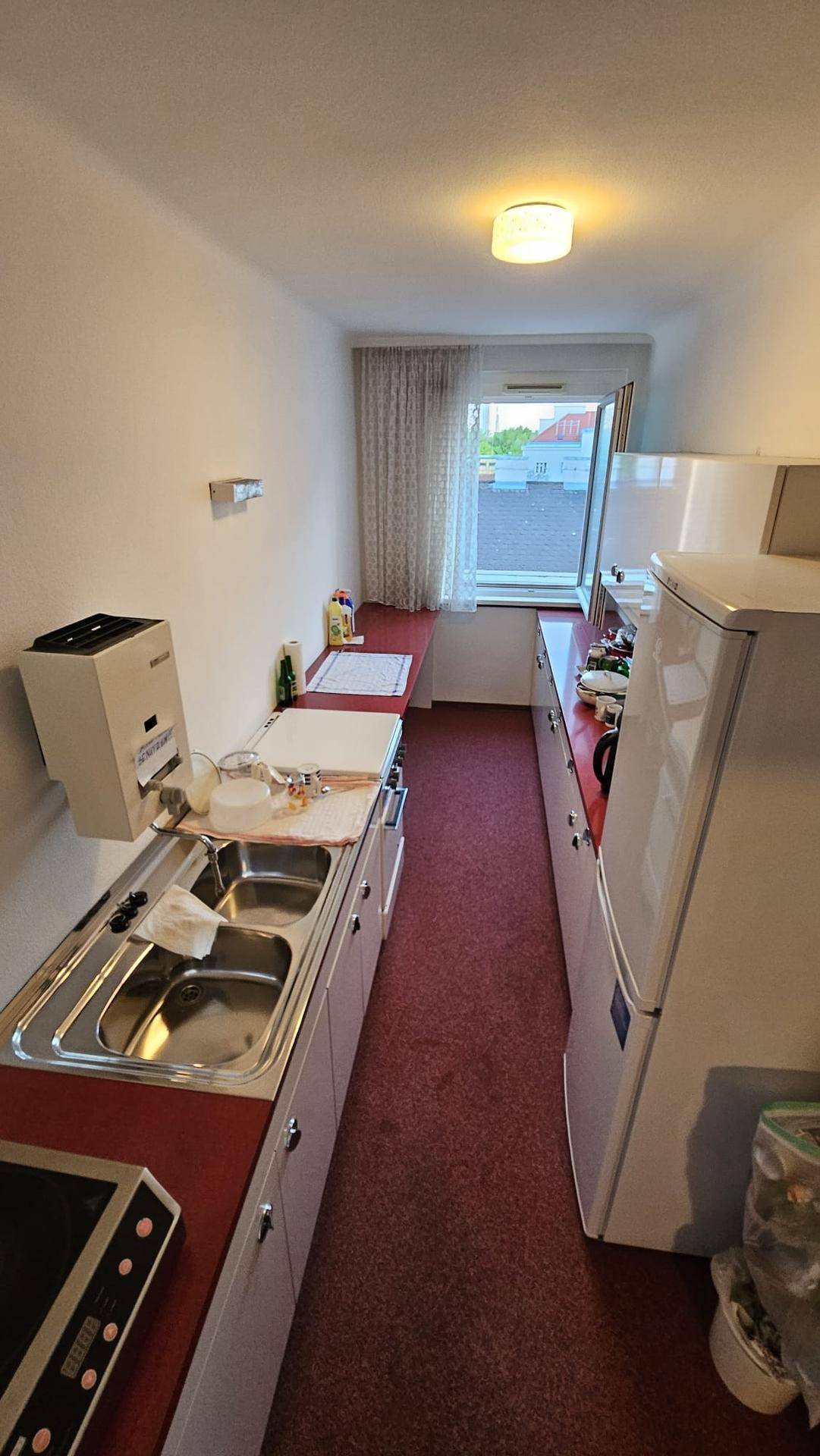 Schmale Küchenzeile mit Spüle, Kühlschrank und Fenster, ideal für kleine Wohnungen.