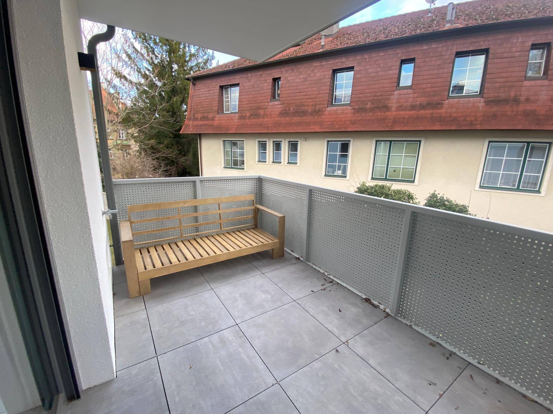 Geräumiger Balkon mit Fliesenboden und einer Holzbank, ideal zum Entspannen.