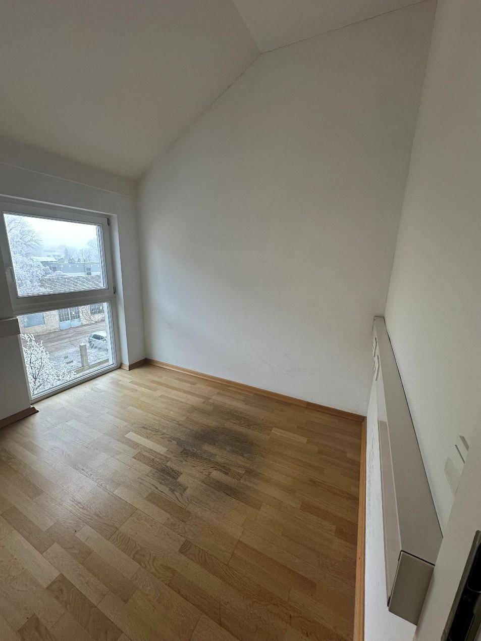 Helles Zimmer mit Holzboden, weißen Wänden und einem großen Fenster mit Blick auf eine verschneite Landschaft.