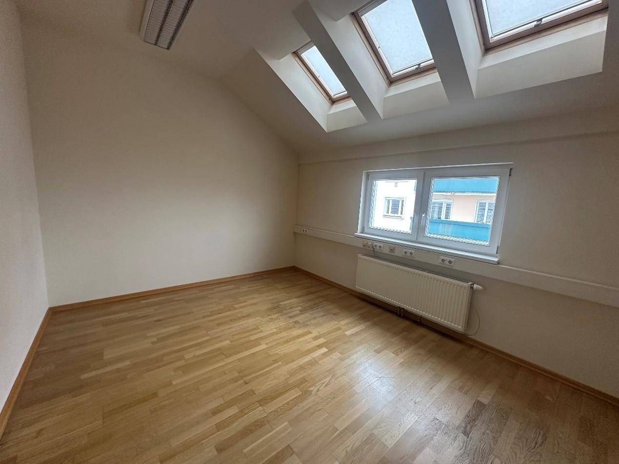 Geräumiges Zimmer mit Holzboden, Dachfenstern und einem Heizkörper, das viel natürliches Licht bietet.