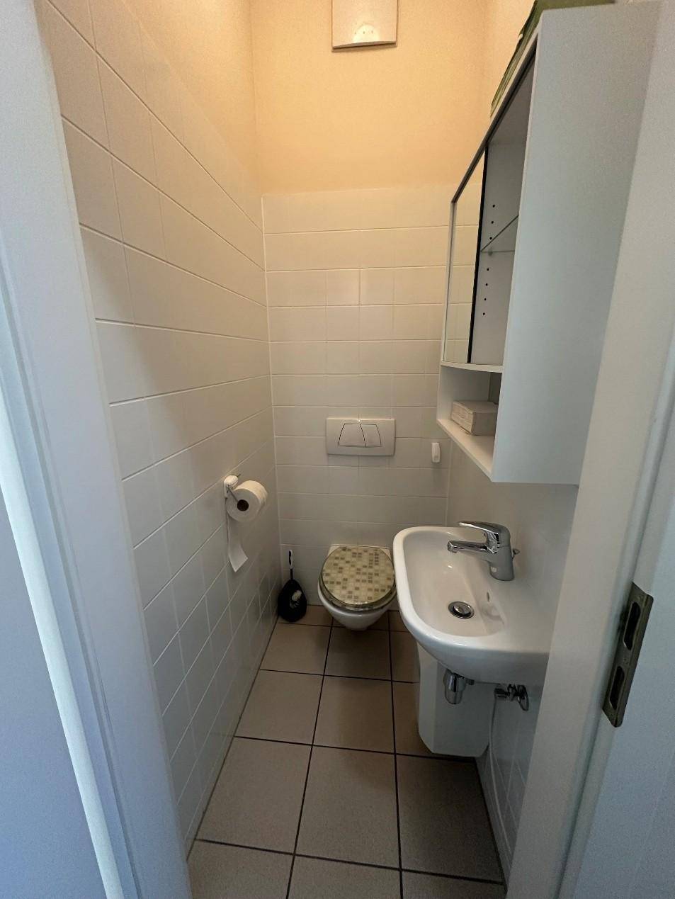 Kleines Gäste-WC mit weißen Fliesen, wandhängender Toilette, Waschbecken und Spiegelschrank.