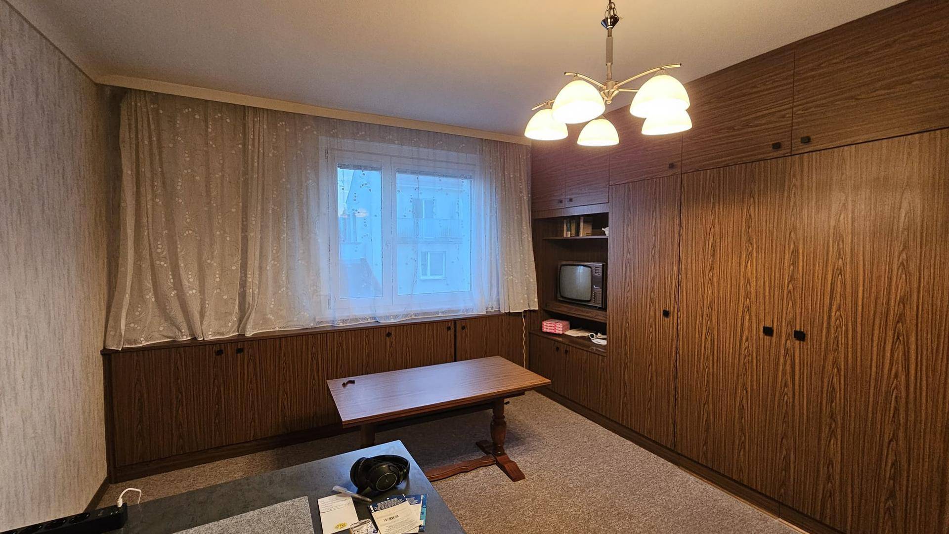 Gemütliches Wohnzimmer mit Holzmöbeln, Teppichboden und einem Fenster mit Vorhängen für Privatsphäre.