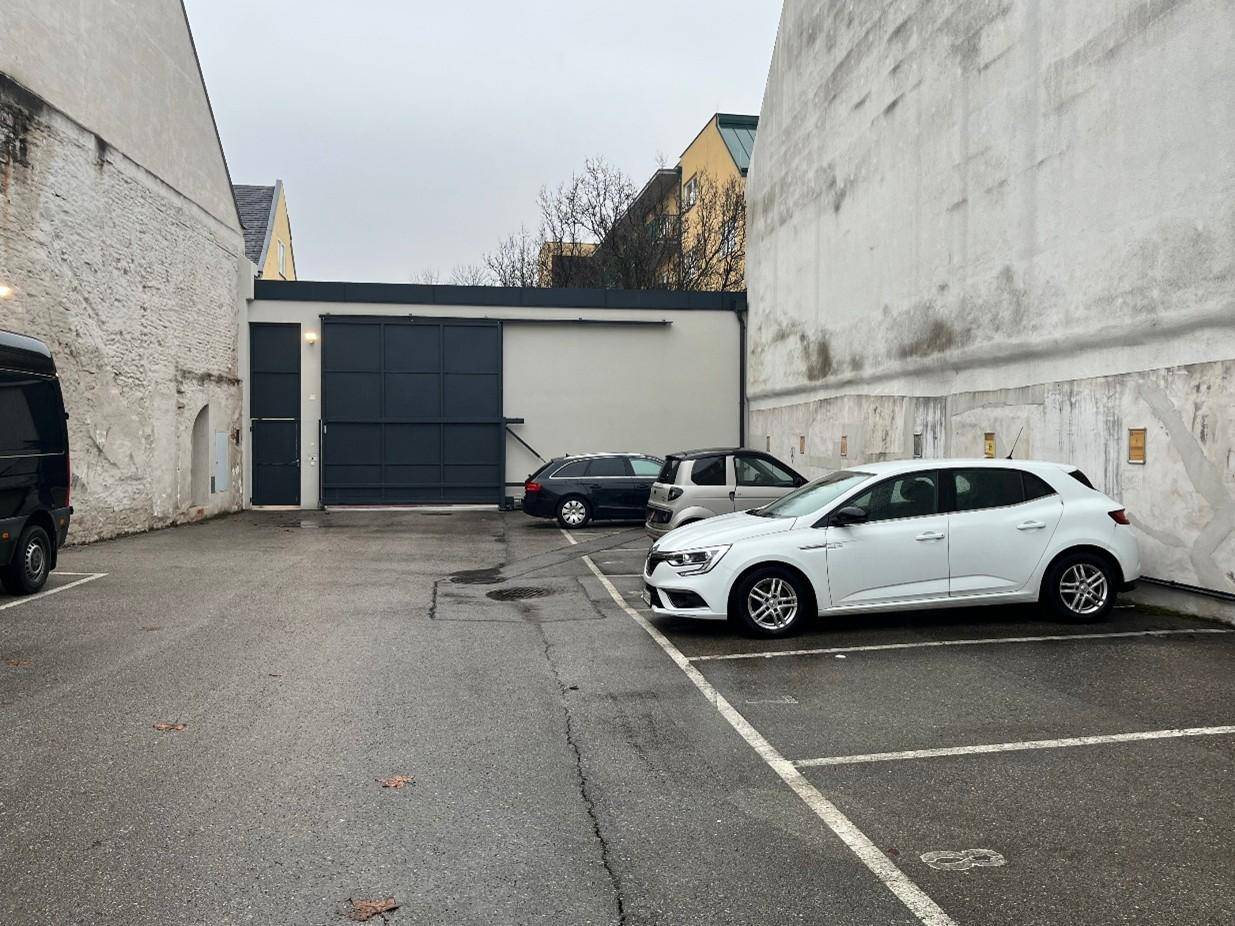 Parkplatz im Freien mit geparkten Autos und einem Garagengebäude im Hintergrund.