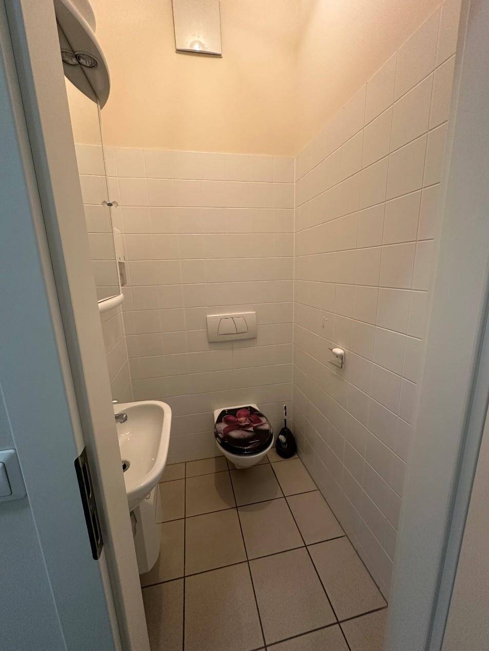 Funktionales Gäste-WC mit weißen Fliesen, wandhängender Toilette und kleinem Waschbecken.