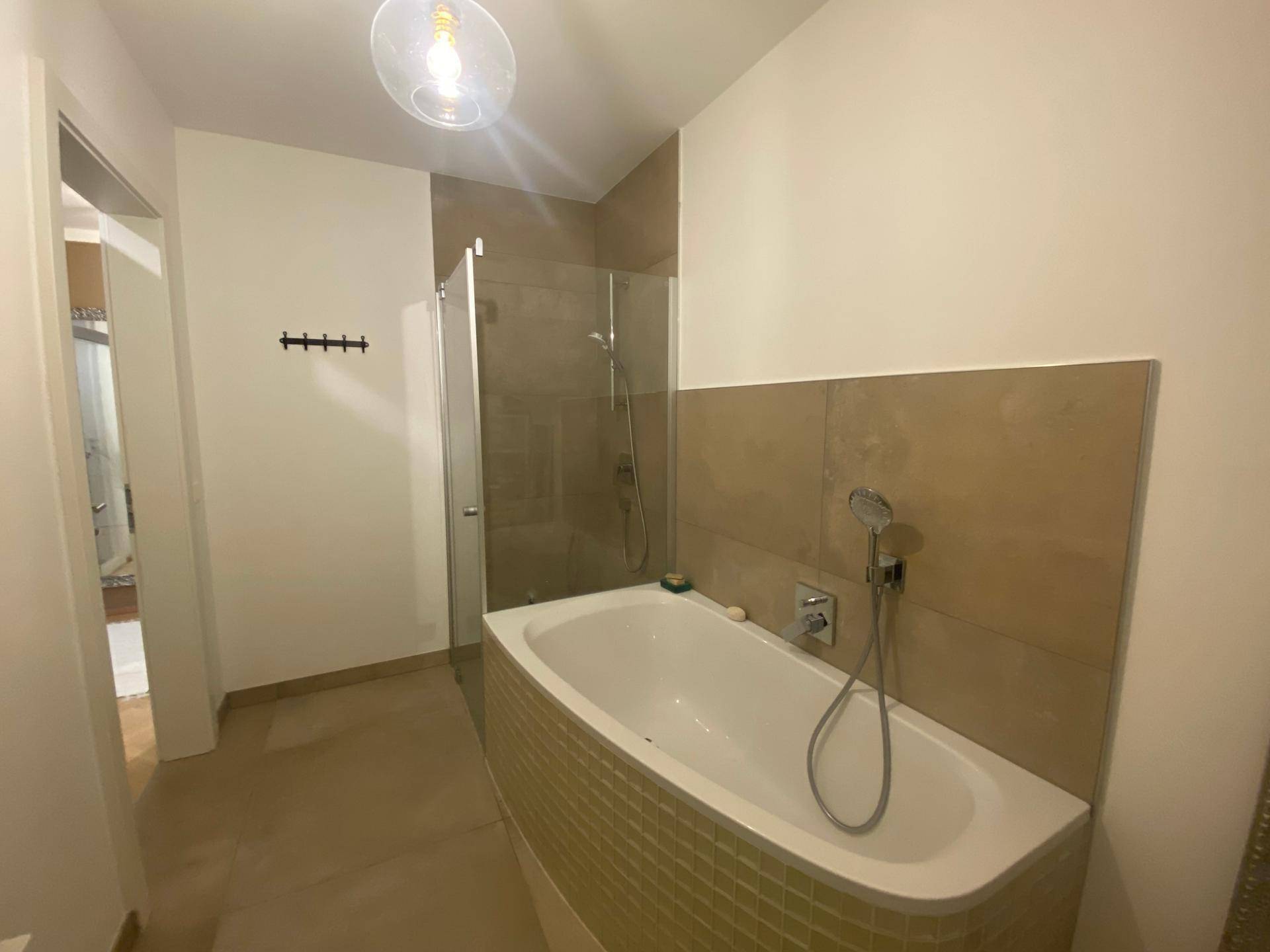 Modernes Badezimmer mit Badewanne und separater Duschkabine, hell gefliest.