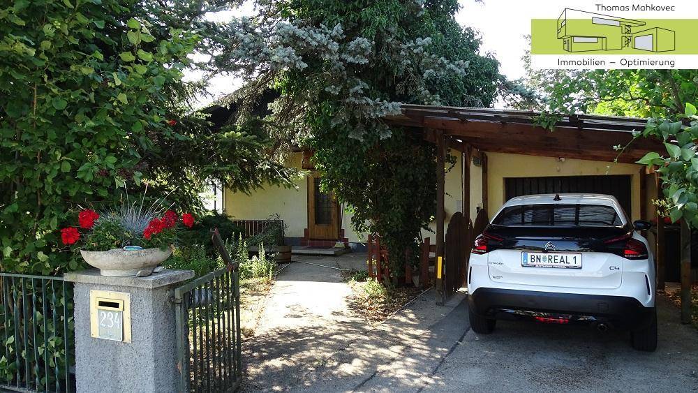 Einfamilienhaus mit gepflegtem Vorgarten, Zufahrt und einem geparkten Auto unter einem Carport.