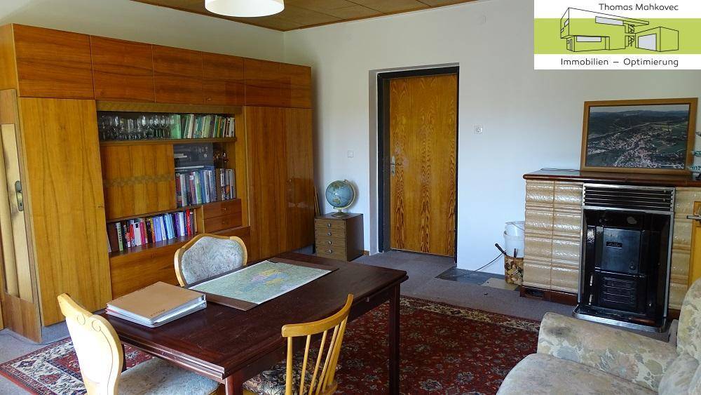 Wohnzimmer mit traditionellem Kachelofen, Holzmöbeln und Teppichboden.