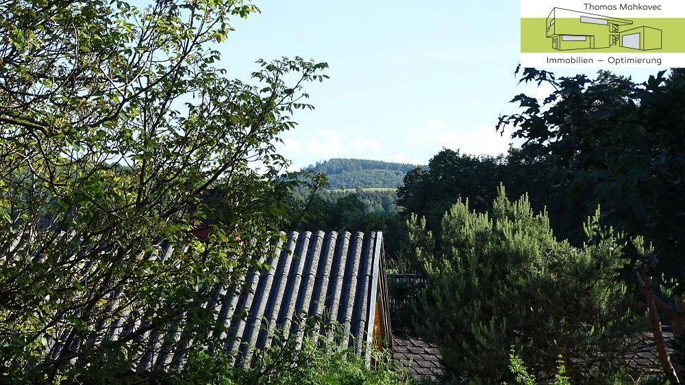 Weitläufiger Blick über ein Dach auf bewaldete Hügel und die umliegende Landschaft.