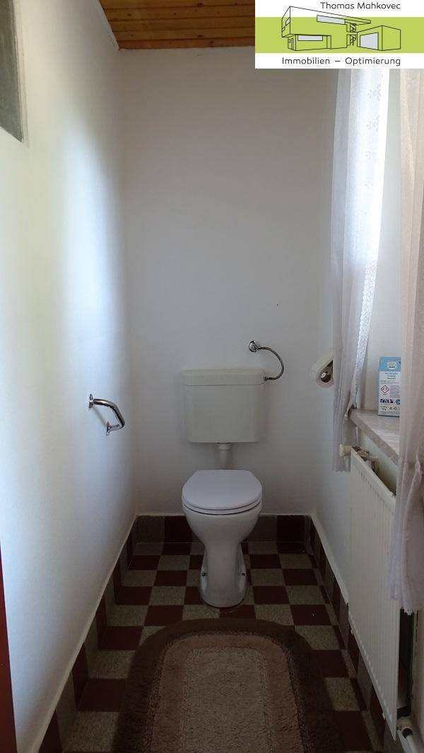 Einfaches WC mit kariertem Fliesenboden und Haltegriffen.
