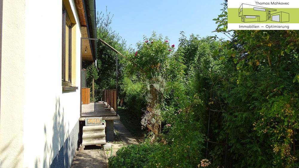 Seitenansicht des Hauses mit einem schmalen Weg und üppiger Bepflanzung.