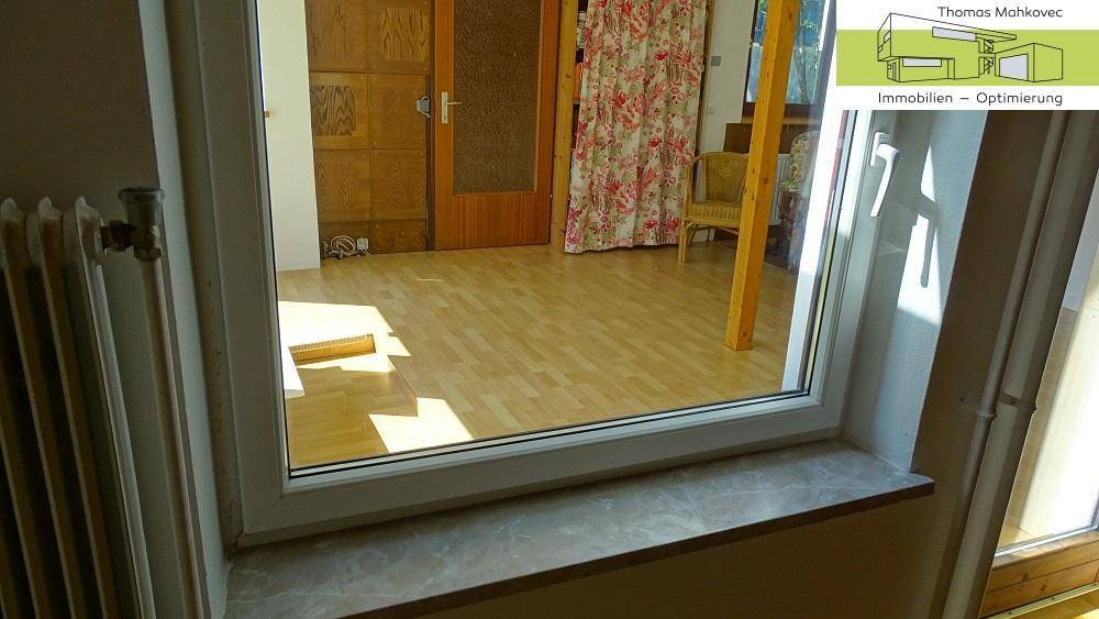 Blick durch ein Fenster auf einen hellen Raum mit Holzfußboden.