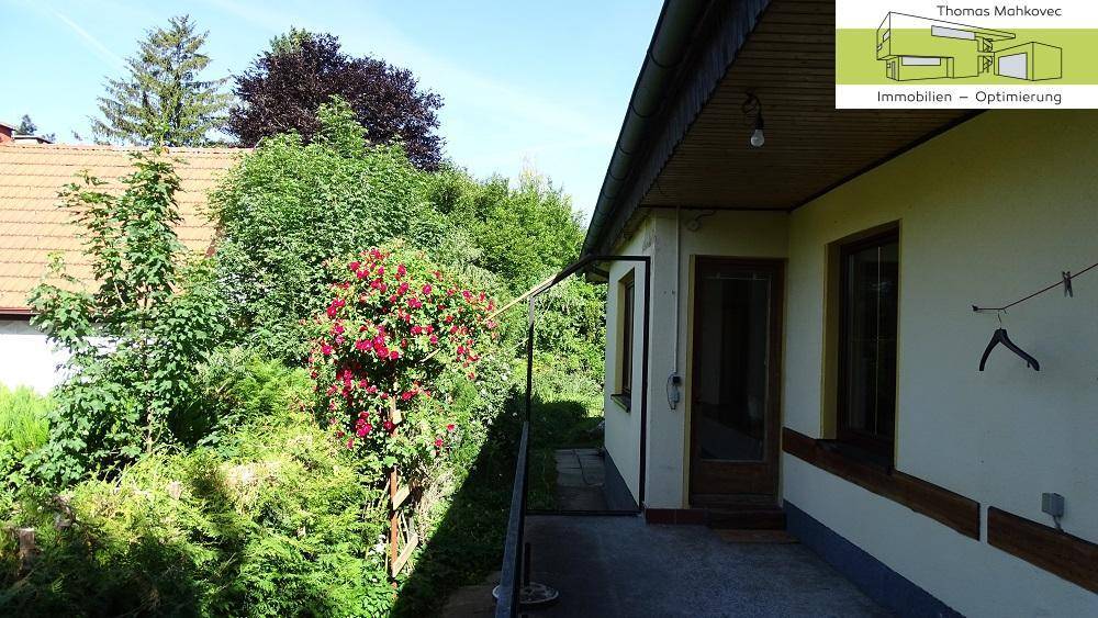 Seitenansicht des Hauses mit einem schmalen Weg und üppiger Bepflanzung.