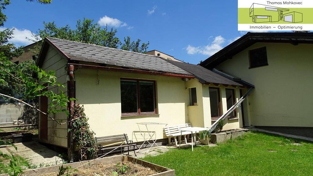 Kleiner Gartenbereich neben dem Haus mit Sitzgelegenheiten und Rasenfläche.