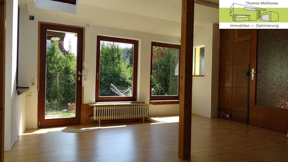 Heller Wohnraum mit großen Fenstern, Holzboden und Zugang zum Außenbereich.