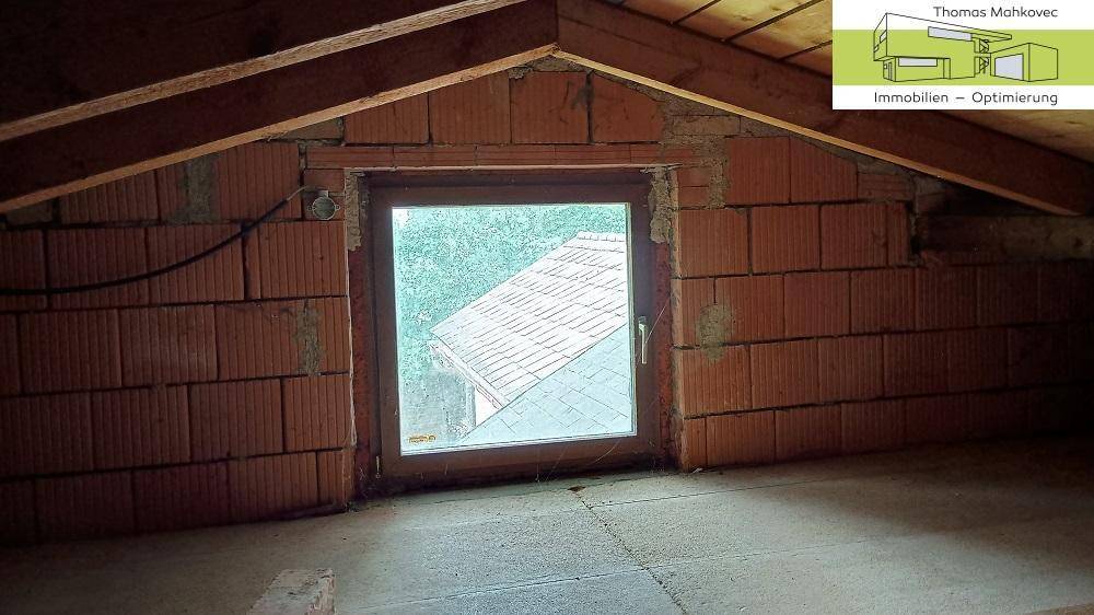 Dachbodenraum mit Fenster, sichtbaren Holzbalken und Ziegelwänden, ideal für Ausbau.