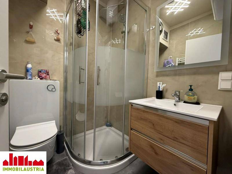 Modernes Badezimmer mit Duschkabine, WC und Waschtischunterschrank in Holzoptik.