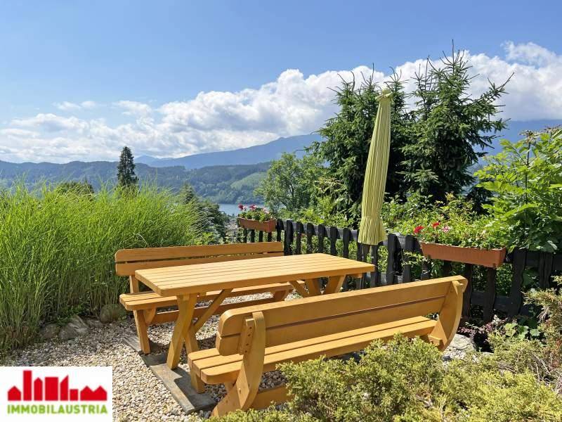 Gemütlicher Sitzbereich im Garten mit Holztisch und Bänken, umgeben von Grün und mit Bergblick.